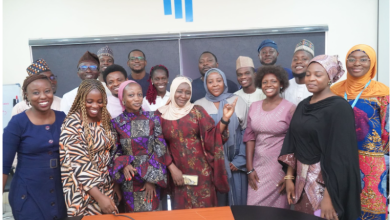A diverse group of people smiling and posing for a photo in a conference room with a logo in the background.