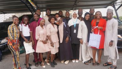 Group of people smiling and posing under a carport, some holding bags.